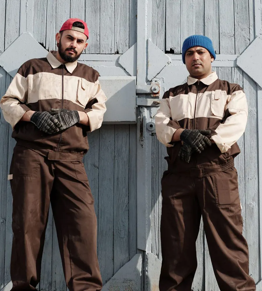 Two workers in matching uniforms and work gloves standing with their arms crossed