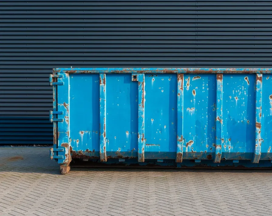 A roll-off dumpster container standing ready on a paved surface