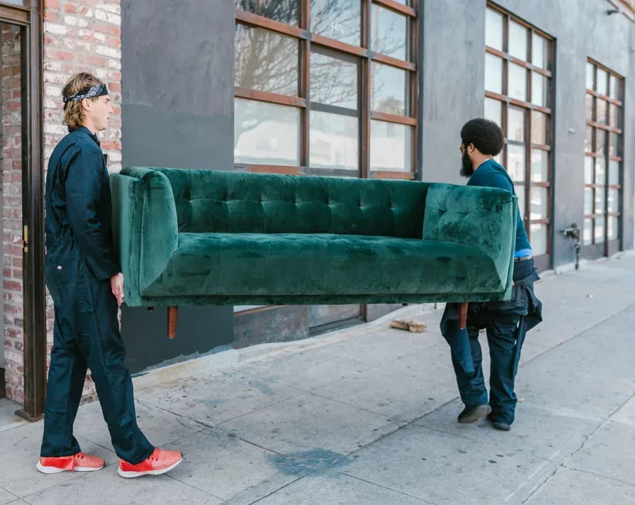 Two workers in overalls carrying a sofa away between them