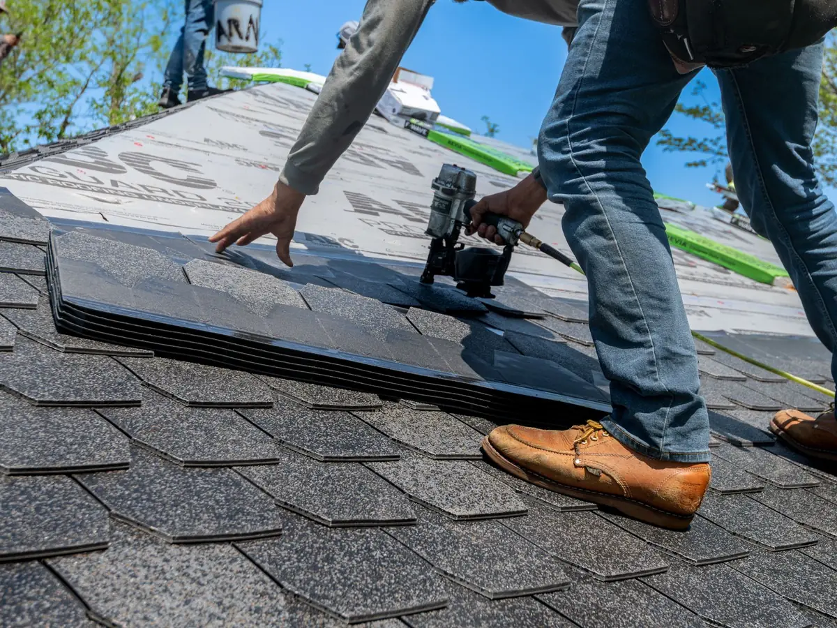 A roofer laying a fresh course of asphalt shingles