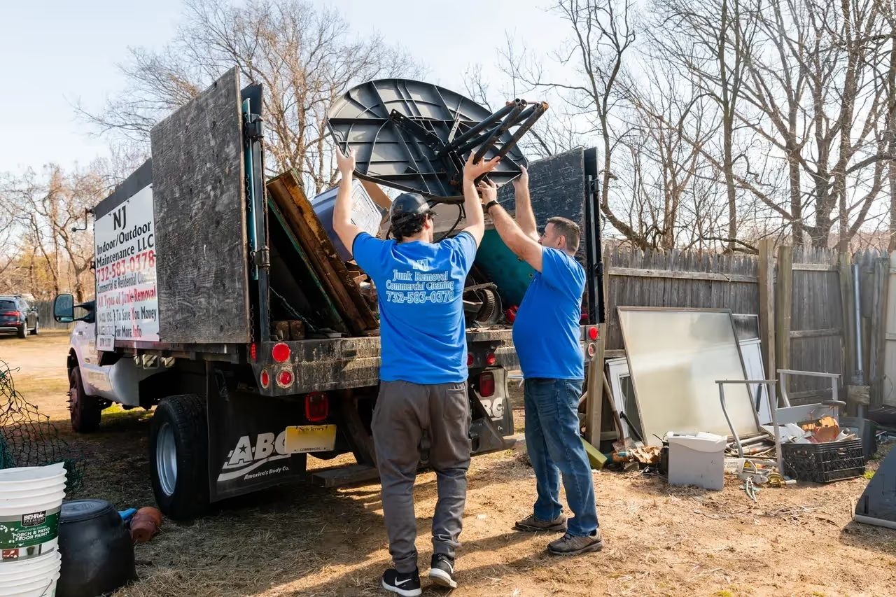 Two crew members lifting a discarded appliance into the truck