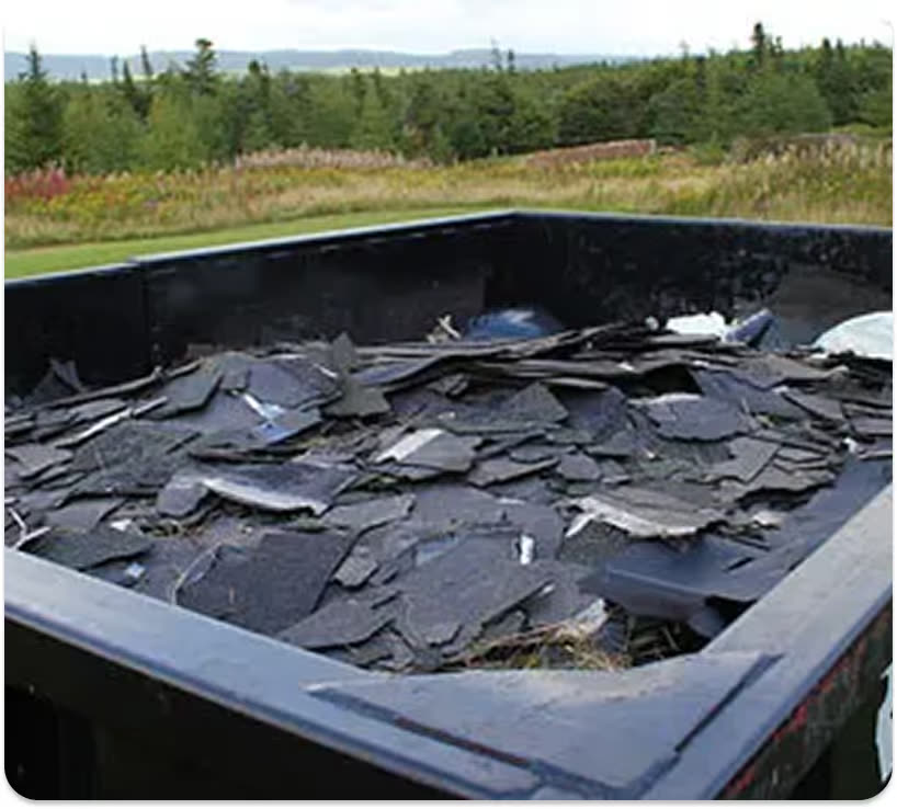 Looking down into a black roll-off dumpster filled with torn-off asphalt roof shingles