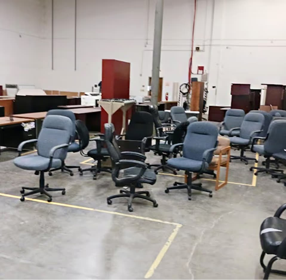 A warehouse floor covered in surplus blue and black office chairs and desks awaiting removal